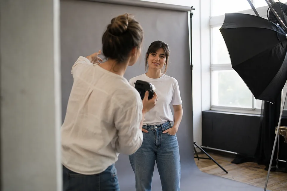 Sesja testowa w studiu, dorosła modelka na szarym tle słucha wskazówek fotografki