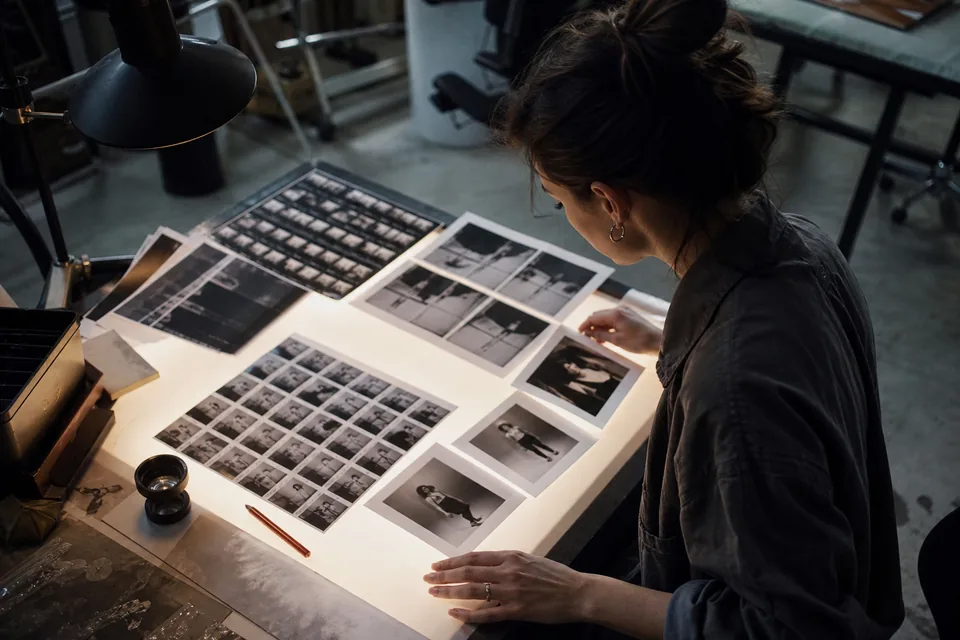 Stół podświetlany w ciemni studia, dłonie fotografa układają wydrukowane stykówki i polaroidy z sesji